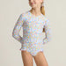 Young girl wearing a floral swimsuit with long sleeves on a plain background