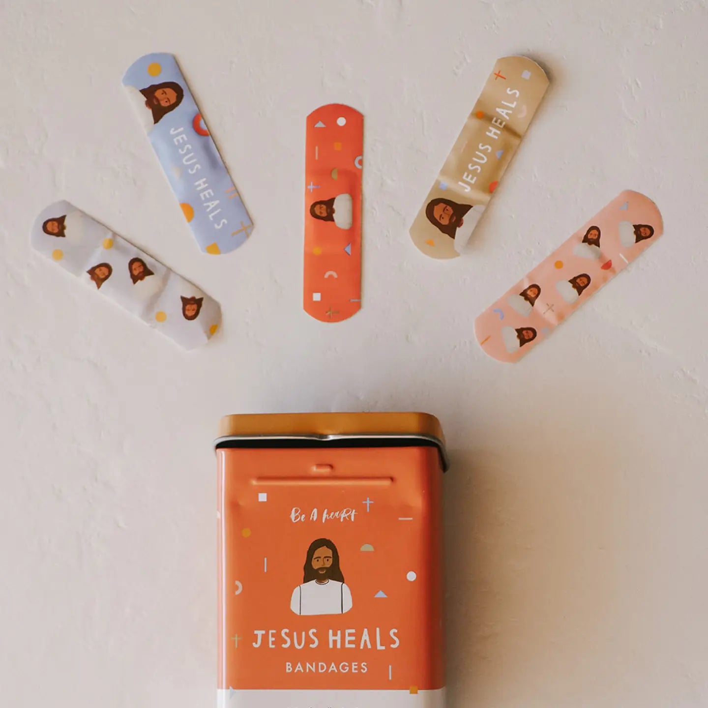 Bandages with 'Jesus Heals' text and a tin labeled 'Jesus Heals Bandages' on a light background