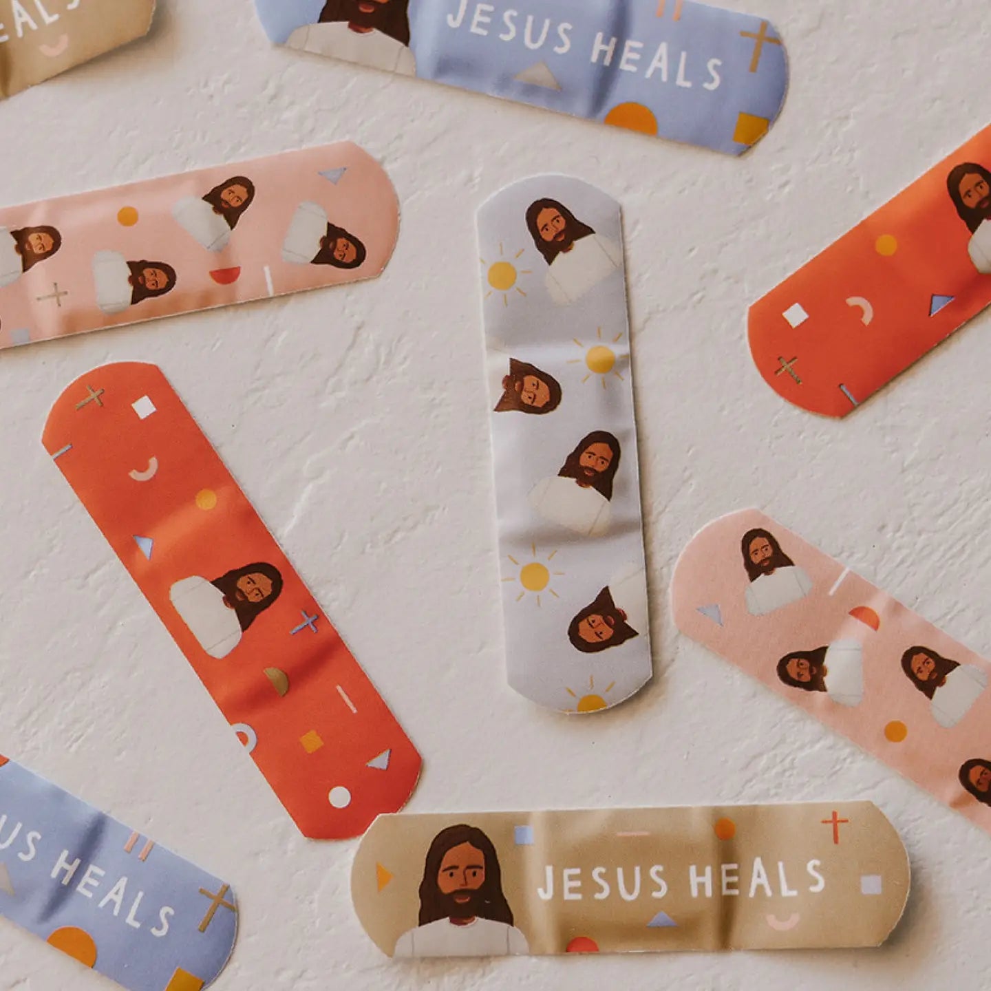 Band-aids with illustrations and 'Jesus Heals' text on a light background