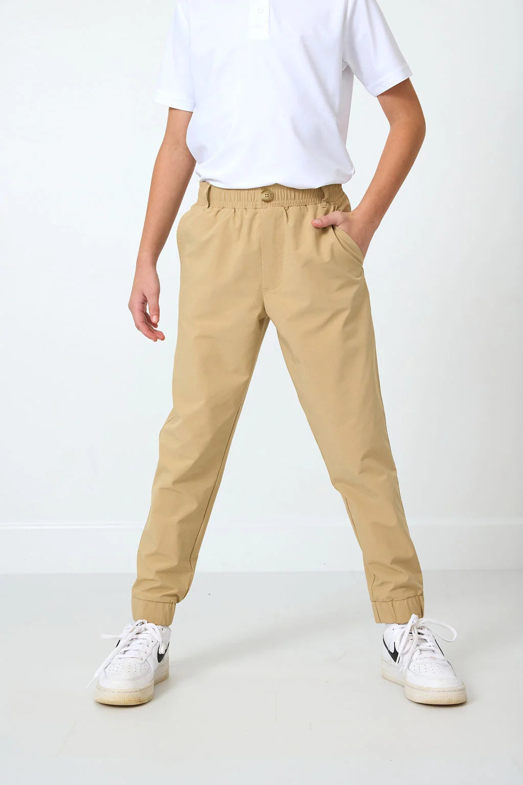 Person wearing beige joggers and white sneakers on a white background