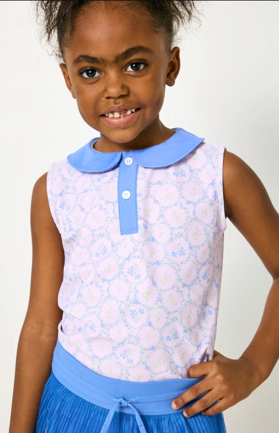 Young girl wearing a sleeveless floral top with a blue collar and matching skirt against a white background