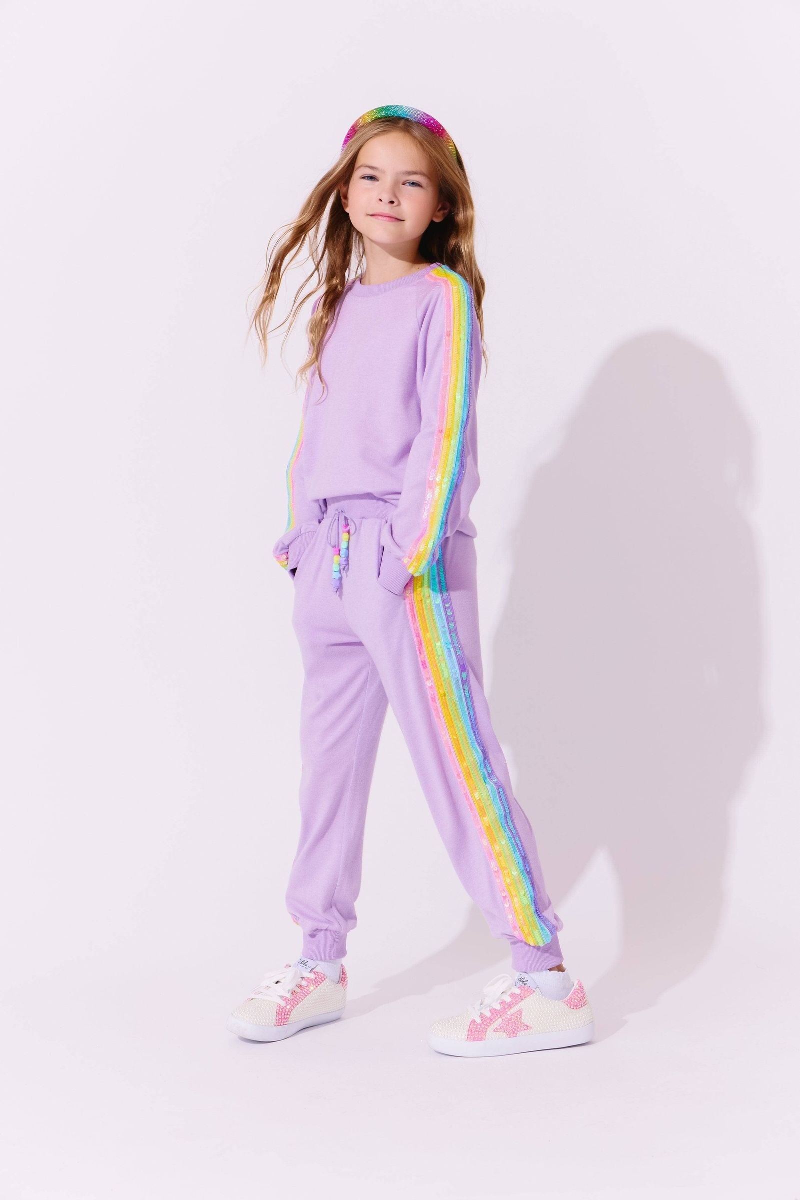 Young girl wearing a lavender tracksuit with rainbow stripes on a white background