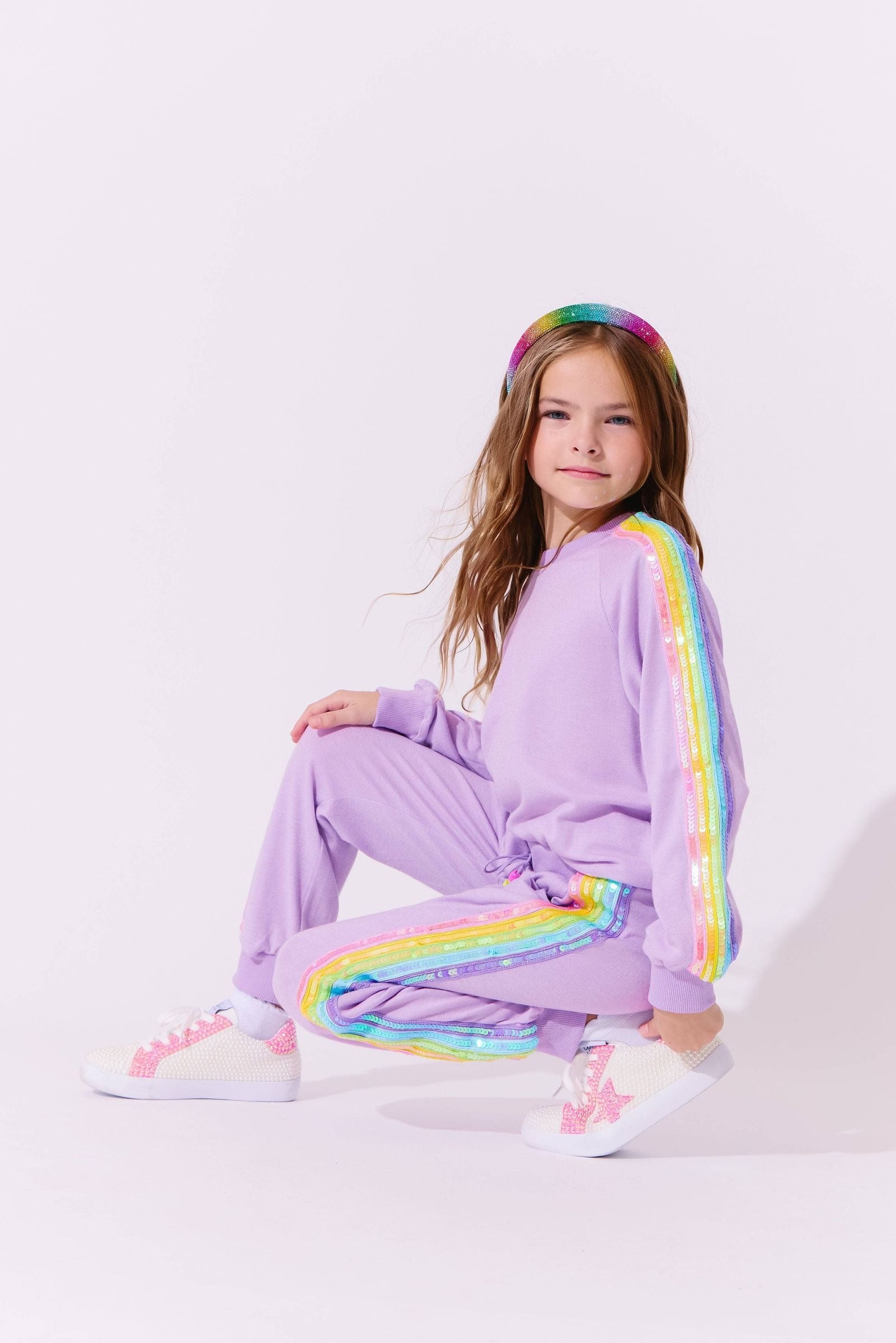 Child wearing a purple track suit with rainbow accents on a white background