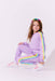 Child wearing a purple track suit with rainbow accents on a white background