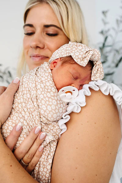 Woman holding a baby wrapped in a patterned blanket with a pacifier.