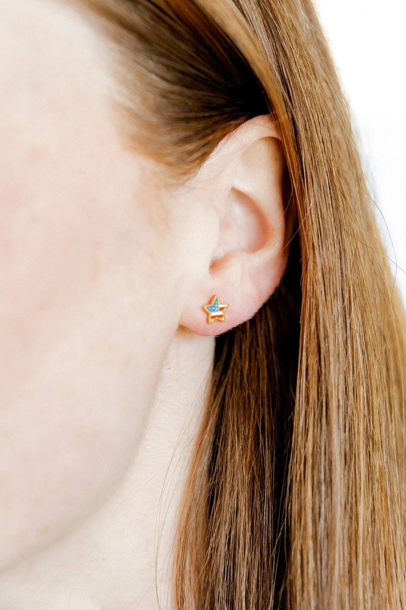 Close-up of an ear wearing a star-shaped earring with blonde hair.