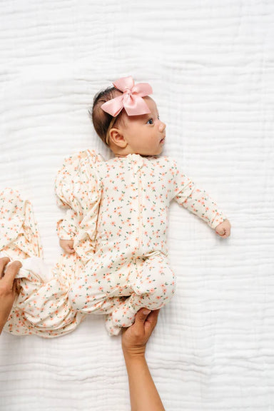 Baby in a floral outfit with a pink bow lying on a white textured surface