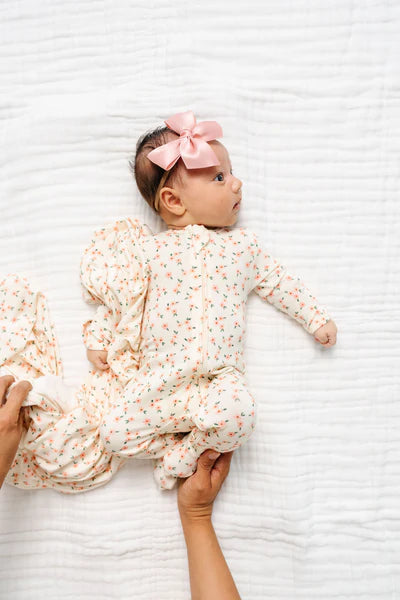 Baby in a floral outfit with a pink bow lying on a white textured surface