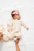 Baby in a floral outfit with a pink bow lying on a white textured surface