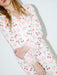 A close-up of a person wearing a white pajama set with a pink cherry and heart print, featuring fluffy light pink feather trim at the cuffs.