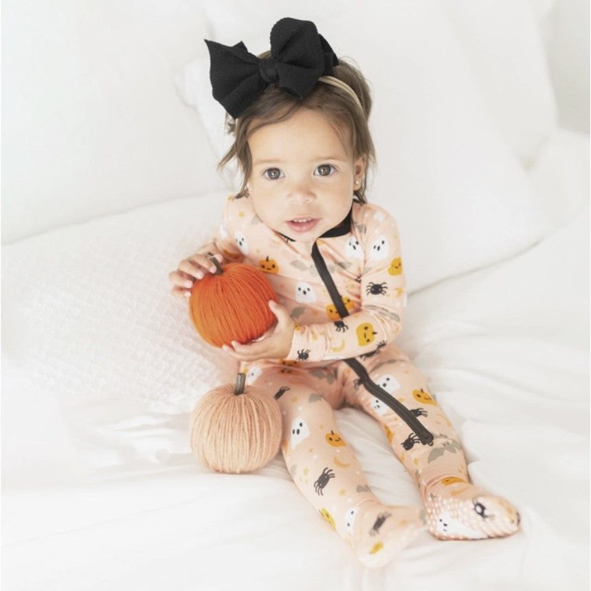 toddler girl wearing orange zippered footie with halloween friends print with pumpkins, ghosts, spiders and bats print