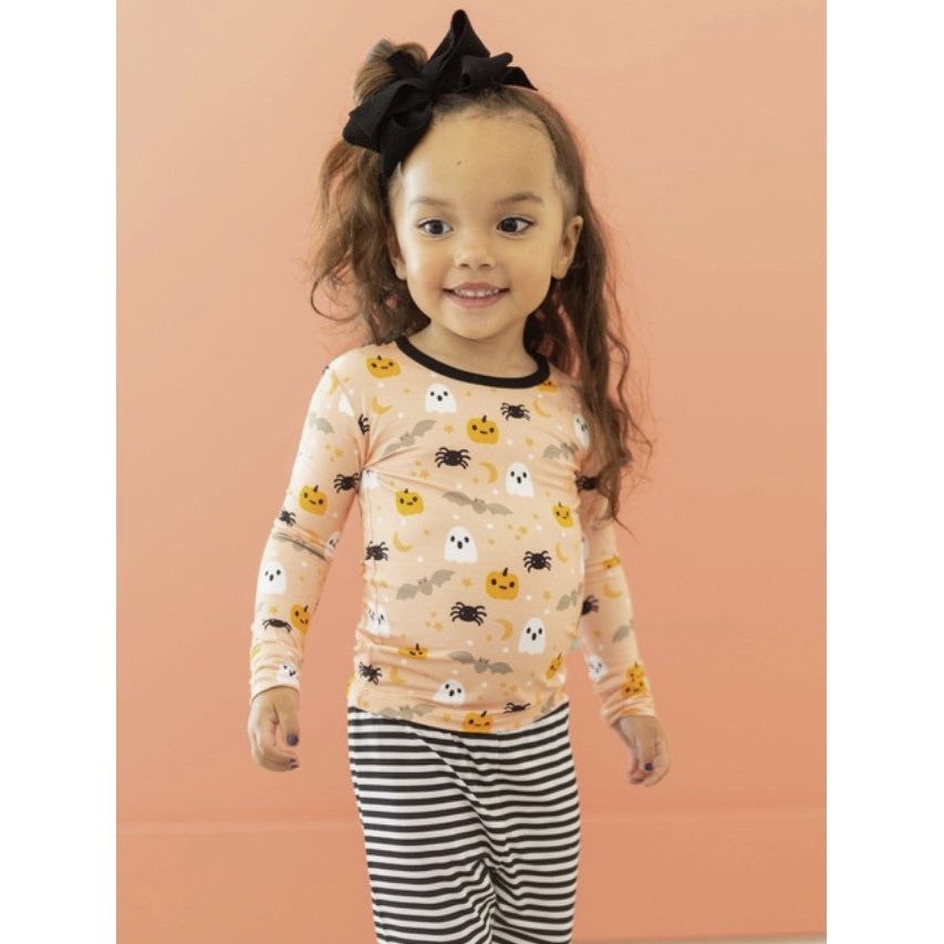 girl wearing two piece loungewear set with orange top with halloween friends print with ghosts, pumpkins, bats and spiders with black and white striped bottoms