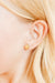 Gold stud earring worn by a person with blonde hair.