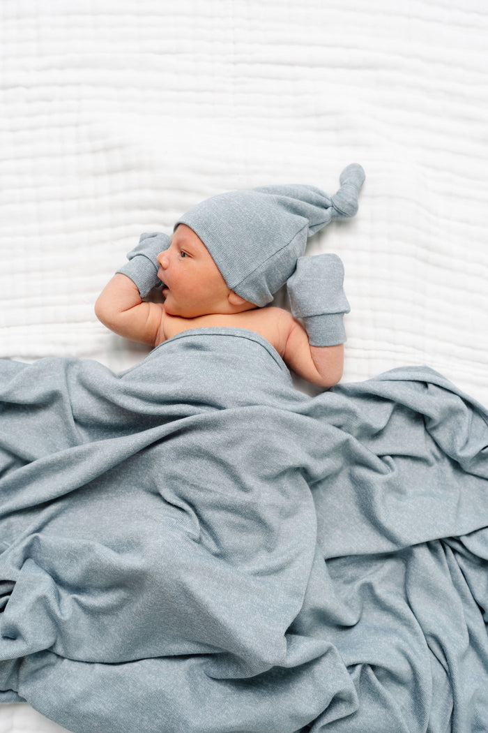 Newborn baby wrapped in a blue blanket and wearing a matching blue hat on a white background