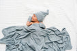 Baby wrapped in a blue blanket and wearing a matching blue hat on a white background