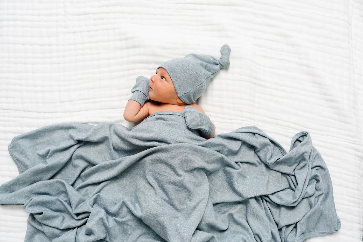 Baby wrapped in a blue blanket and wearing a matching blue hat on a white background