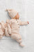 A sleeping newborn baby wearing a matching beige and white gingham footed sleeper and hat, lying on a white textured muslin blanket.