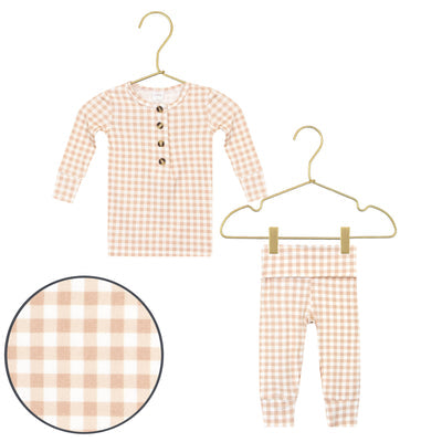 A two-piece baby outfit set featuring a long-sleeve henley top and matching pants in a light peach and white gingham check pattern, displayed on gold hangers with a circular detail inset of the fabric pattern.
