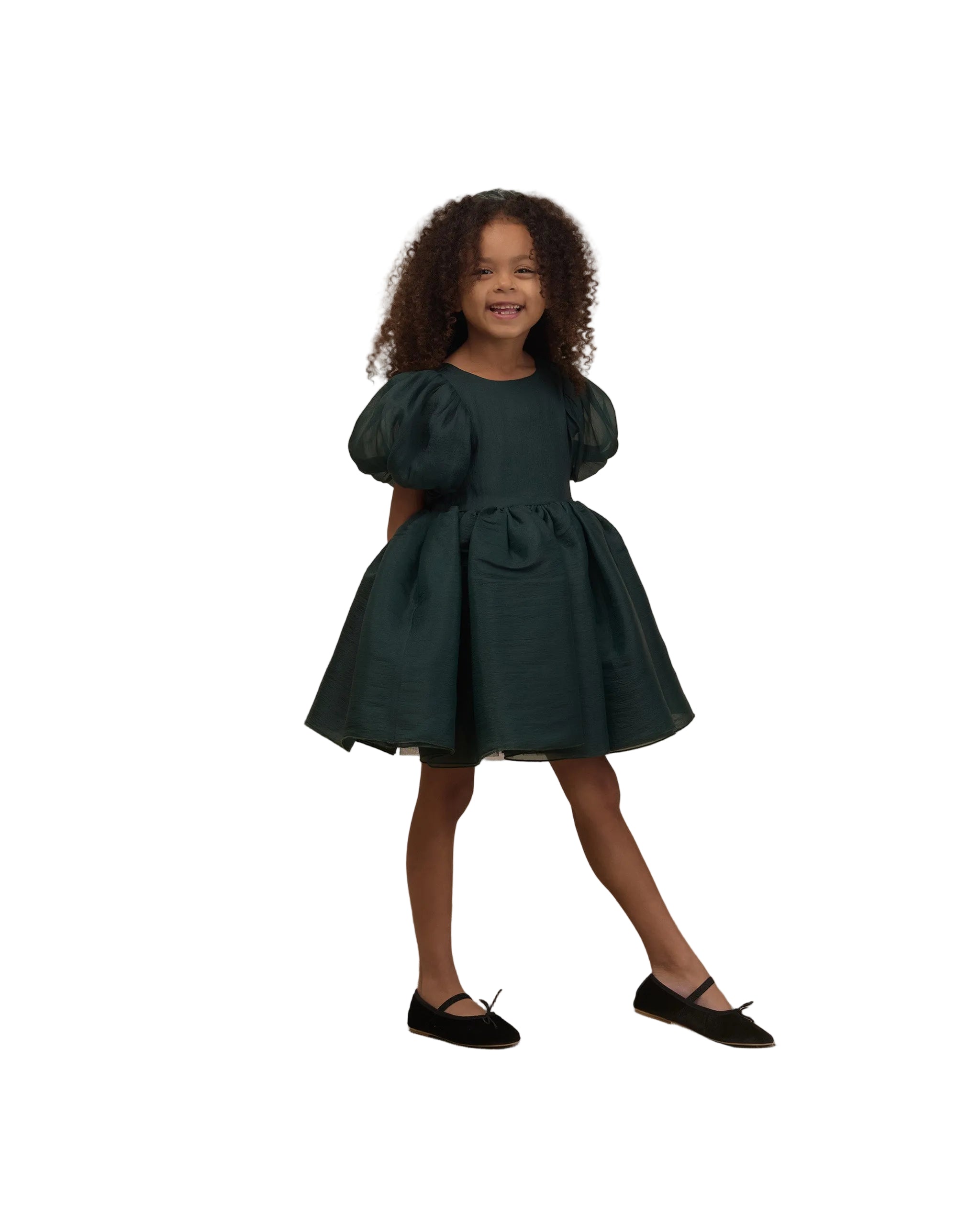 Young girl wearing a dark green shimmer dress with puff sleeves and a full skirt paired with black Mary Jane shoes on a white background from Noralee