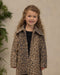 Young girl wearing a Noralee leopard print coat with a full collar and hidden snaps over a black outfit posed indoors beside greenery