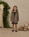 Young girl wearing a leopard print faux fur coat with a full collar and pockets while standing indoors beside holiday greenery and wrapped gifts by Noralee