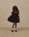 Young girl wearing a Noralee black floral dress with a lace trimmed round collar puff sleeves and full skirt with white socks and Mary Jane shoes