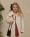 Young girl wearing a cream faux fur coat over a red dress with a black bow and shoulder bag in a cozy holiday setting by Noralee