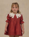 Young girl wearing a ruby red Noralee dress with a scalloped white embroidered collar puff sleeves pleated details and a delicate scalloped hem