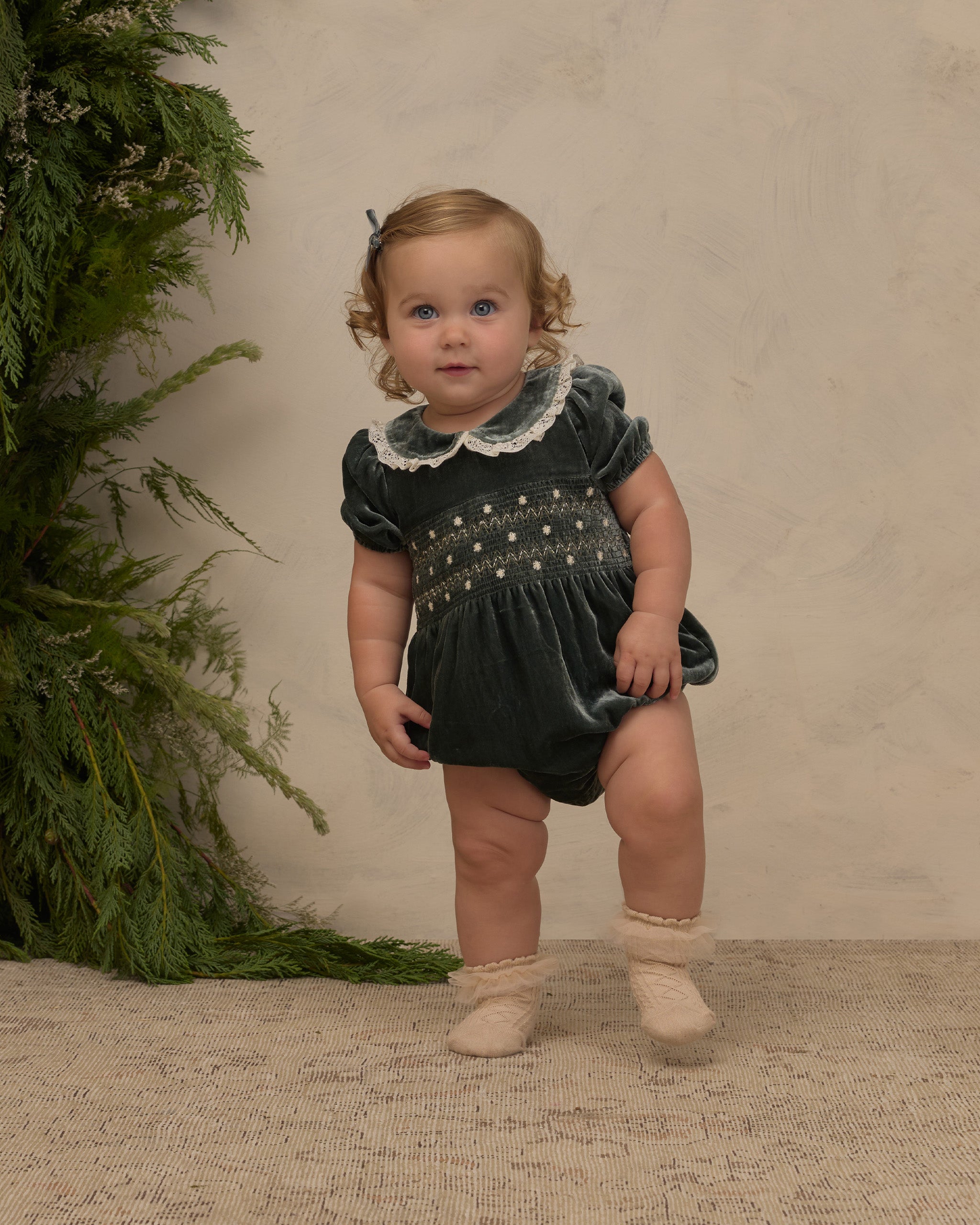 A little girl wearing a green velvet romper with delicate embroidered details.