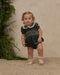 A little girl wearing a green velvet romper with delicate embroidered details.