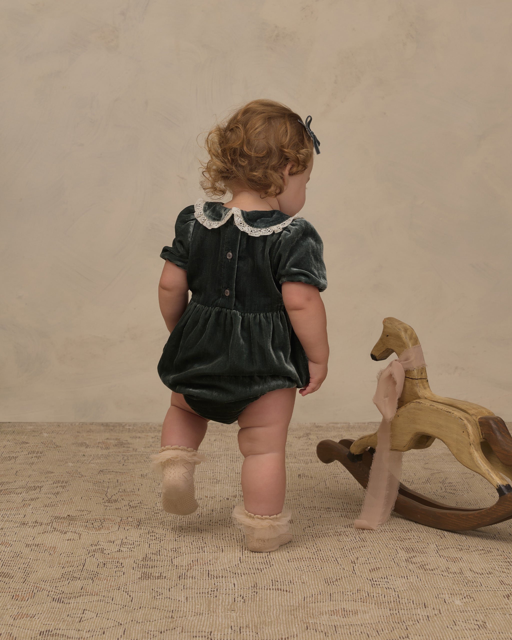 The back of a little girl wearing a green velvet romper with delicate embroidered details.