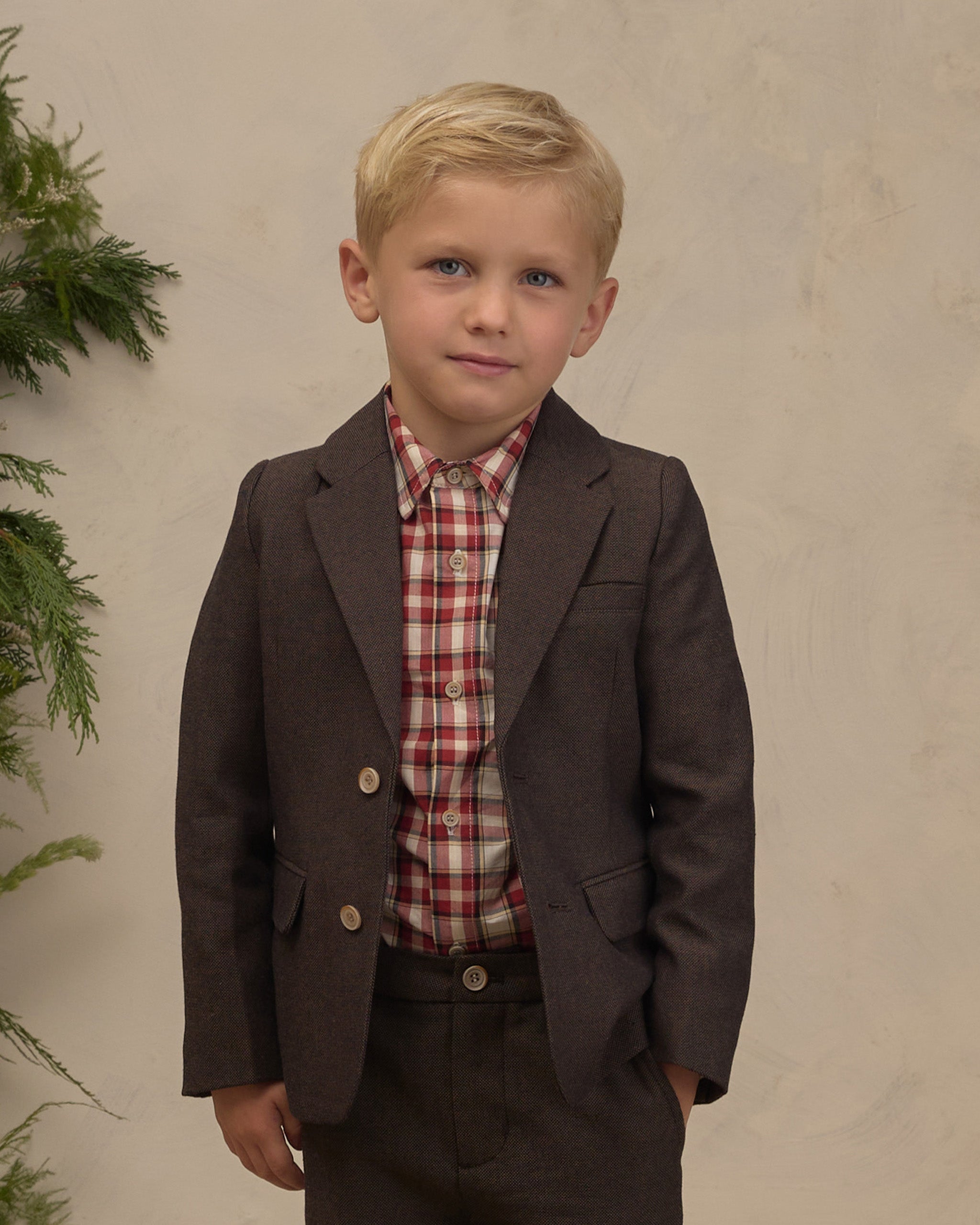 Young boy modeling a dark heathered plaid blazer with notched lapels and front pockets over a red plaid shirt with coordinating trousers from Noralee