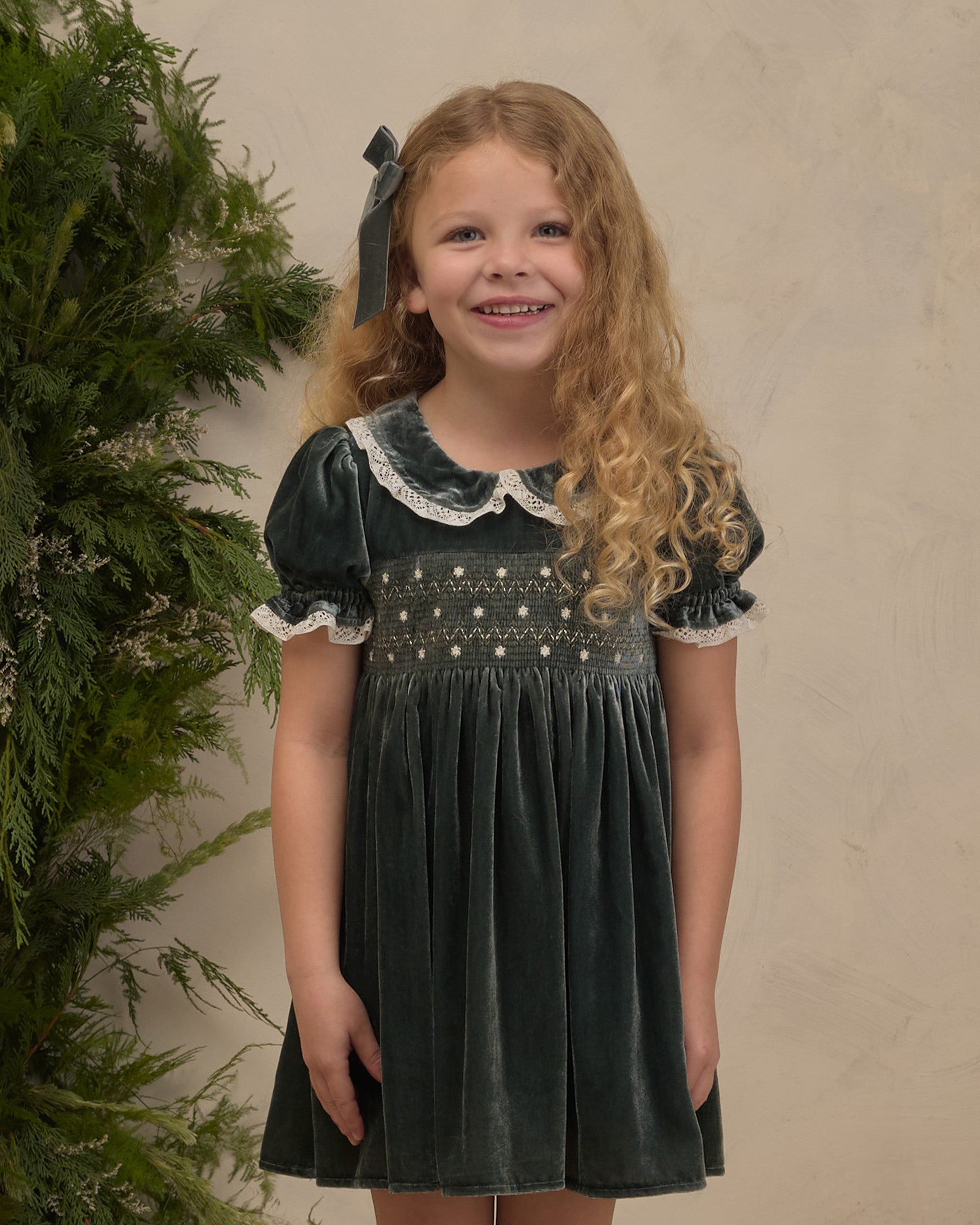 A girl in a green velvet dress with embroidered bodice and lace around the neck and sleeves.