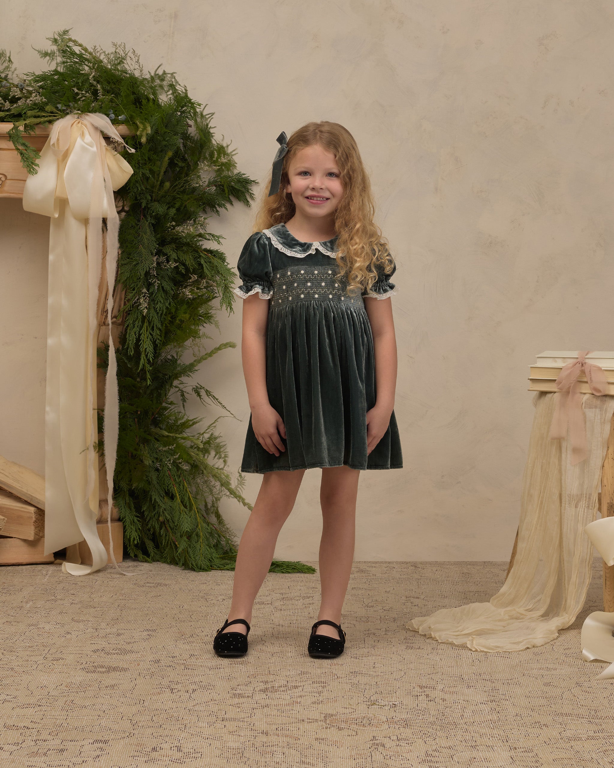 A green velvet dress featuring a smocked bodice, puff sleeves with lace trim, and a scalloped lace Peter Pan collar.