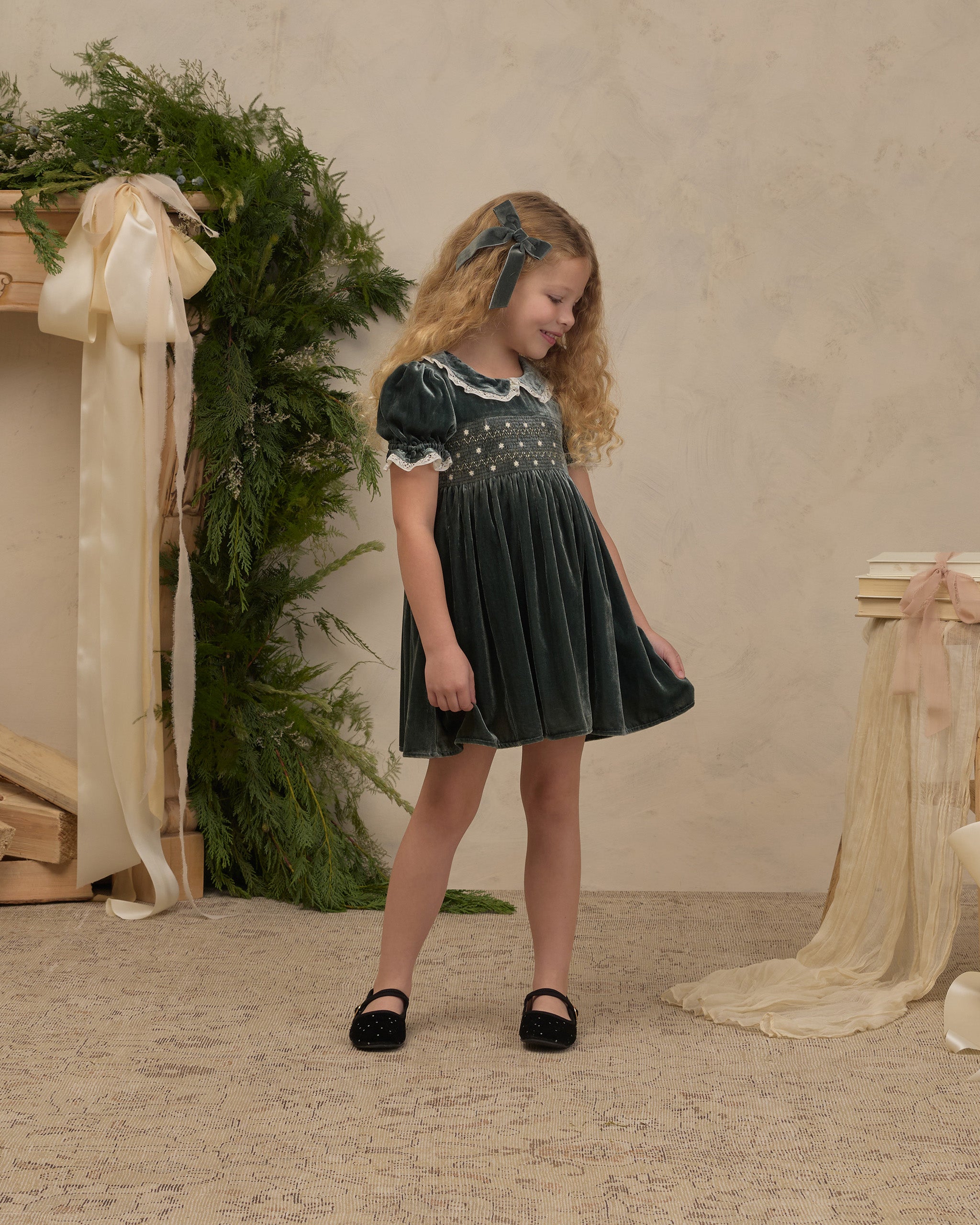 A green velvet dress featuring a smocked bodice, puff sleeves with lace trim, and a scalloped lace Peter Pan collar.