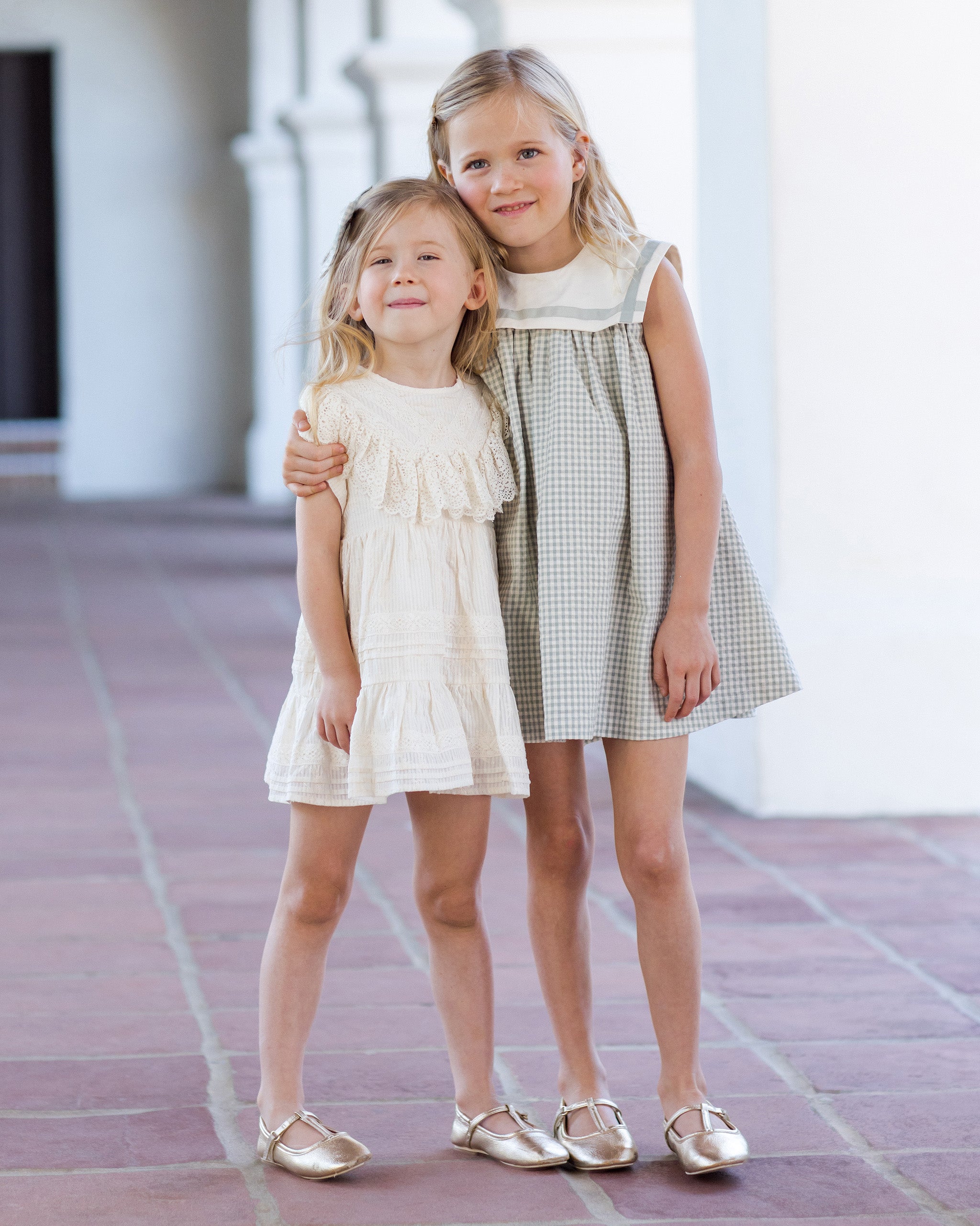 Two young girls in dresses standing together on a tiled floor.