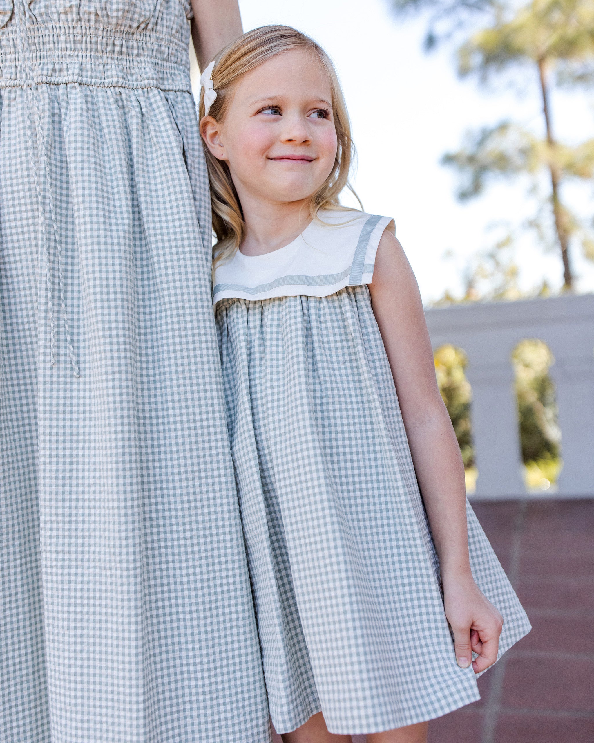 Two children wearing matching green checkered dresses outdoors.