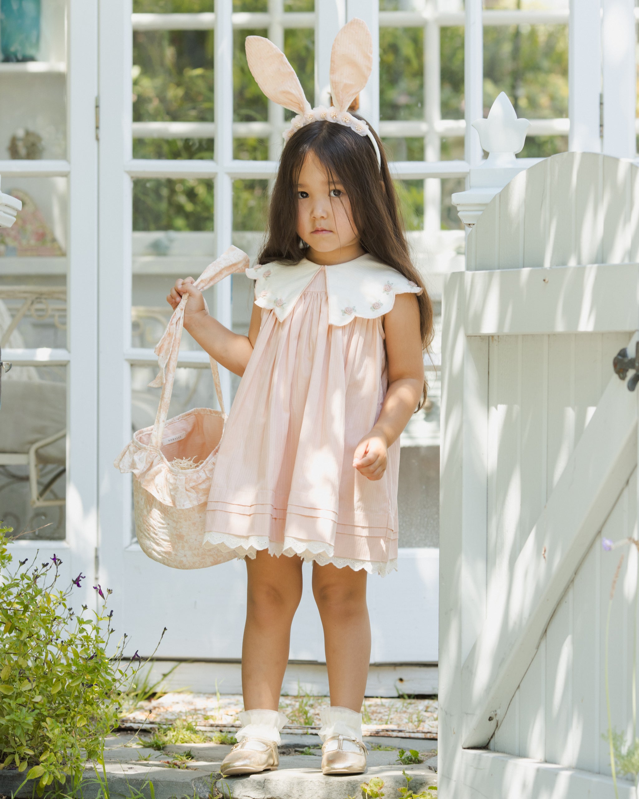 Young girl in a pink dress with bunny ears standing outdoors.