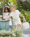 Two children in a garden setting, one with bunny ears and a white bag, the other in a white dress.