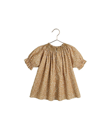 A short-sleeve baby dress with a beige and white floral pattern, featuring puff sleeves and a smocked neckline, hanging on a wooden hanger against a white background.