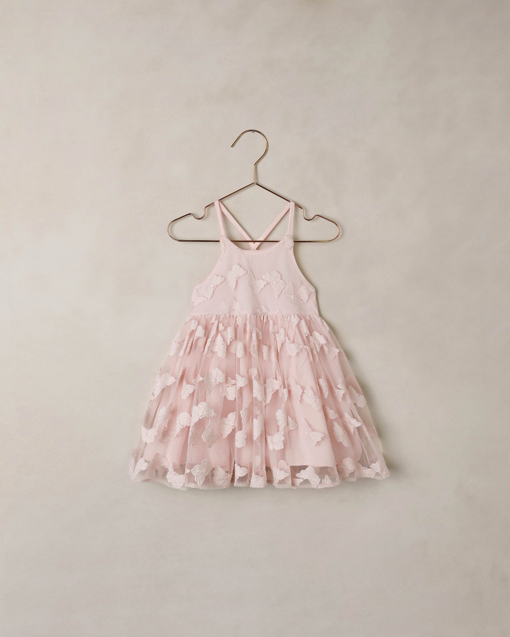 Pink floral dress on a hanger against a beige wall