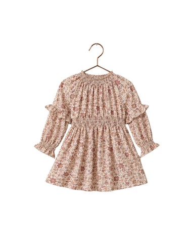 A long-sleeve girl's dress with a delicate pink and brown floral print, featuring a smocked waist and ruffled sleeves, hanging on a wooden hanger against a white background.