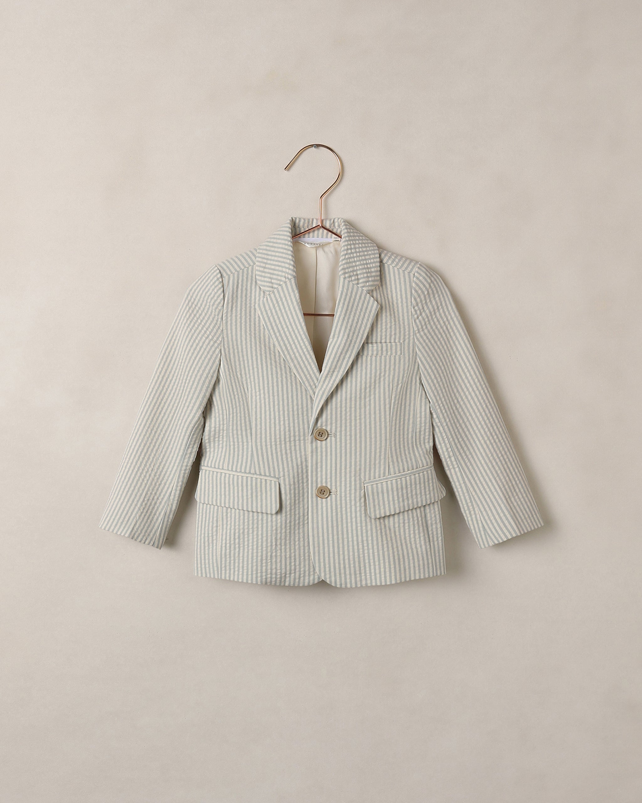 Blue and white striped blazer on a hanger against a beige background