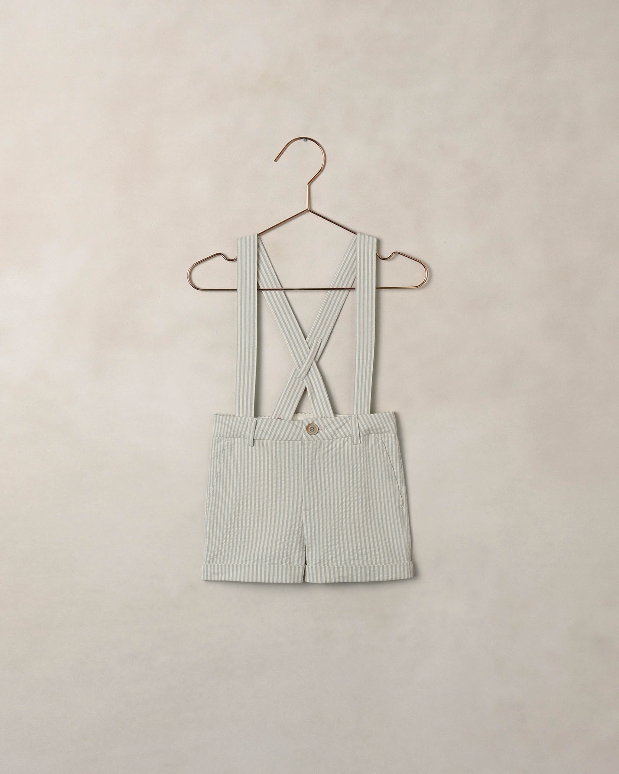 Striped shorts with suspenders on a hanger against a beige background