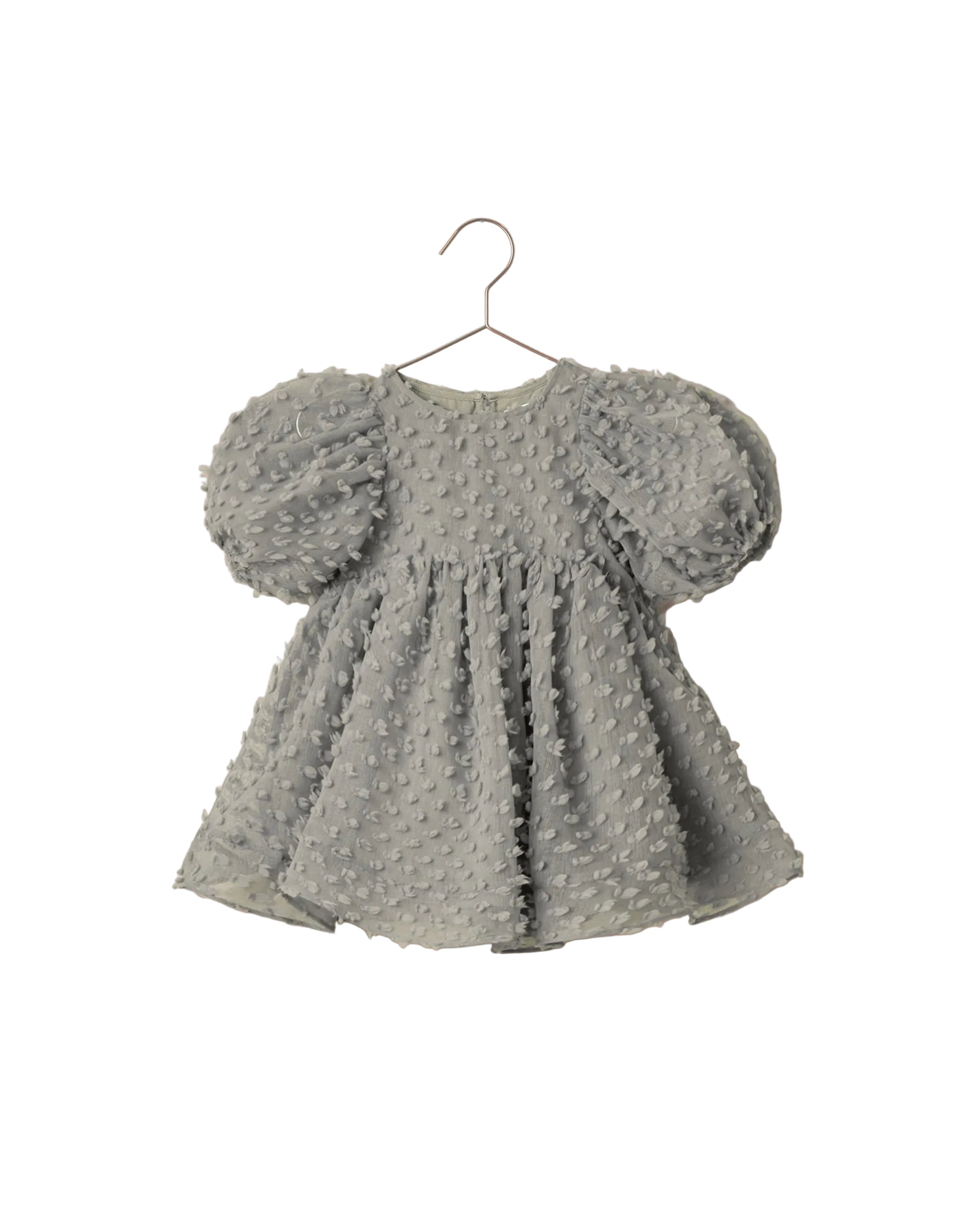 A light green baby dress with textured, raised dots and puffy short sleeves, hanging on a metal hanger against a white background.