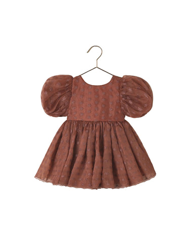 A toddler girl's terracotta-colored dress with puff sleeves and a subtle floral pattern, hanging on a metal hanger against a white background.