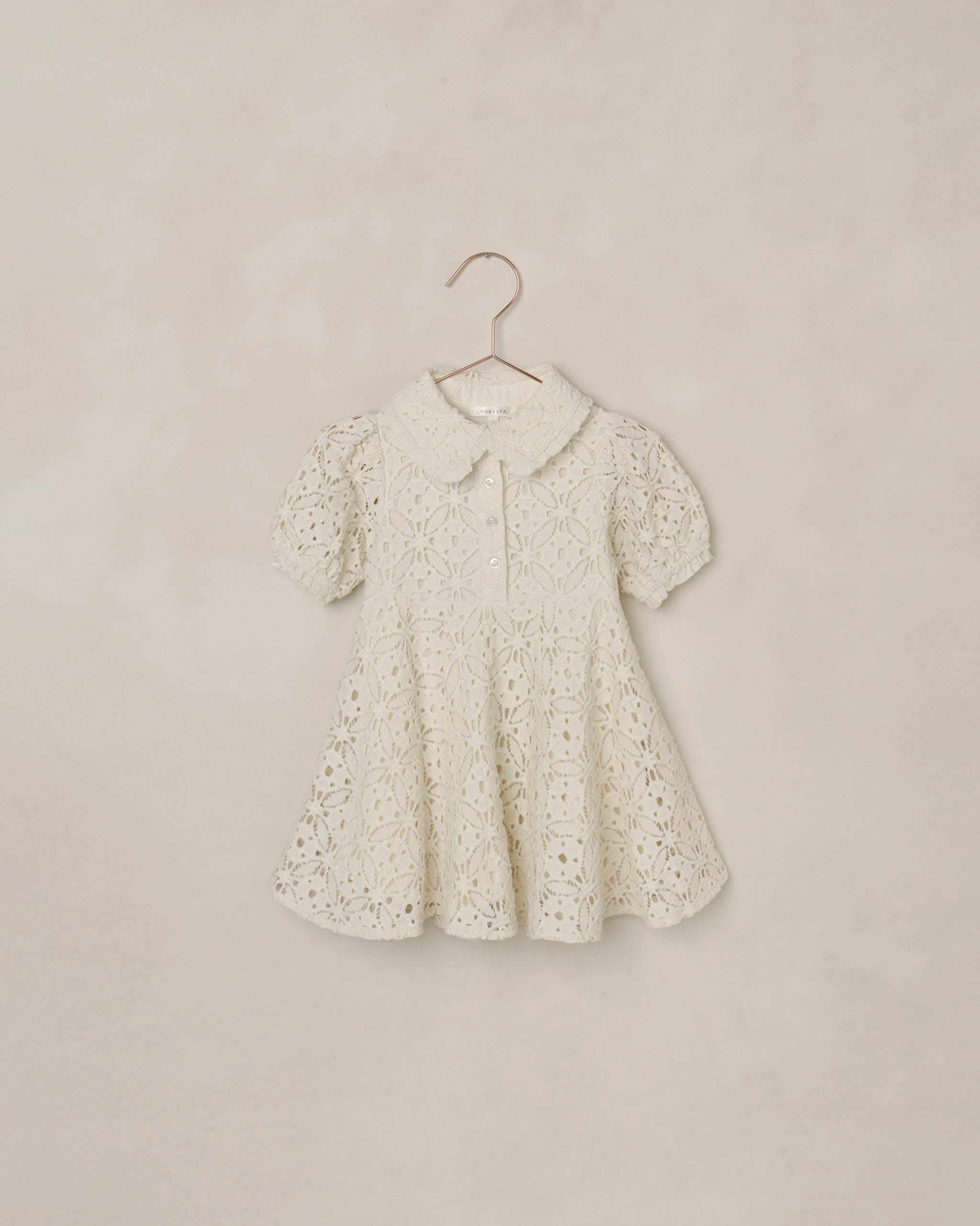 White eyelet lace dress on a hanger against a beige background
