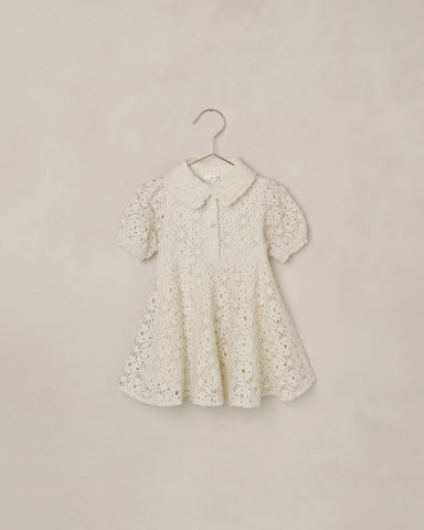 White eyelet lace dress on a hanger against a beige background