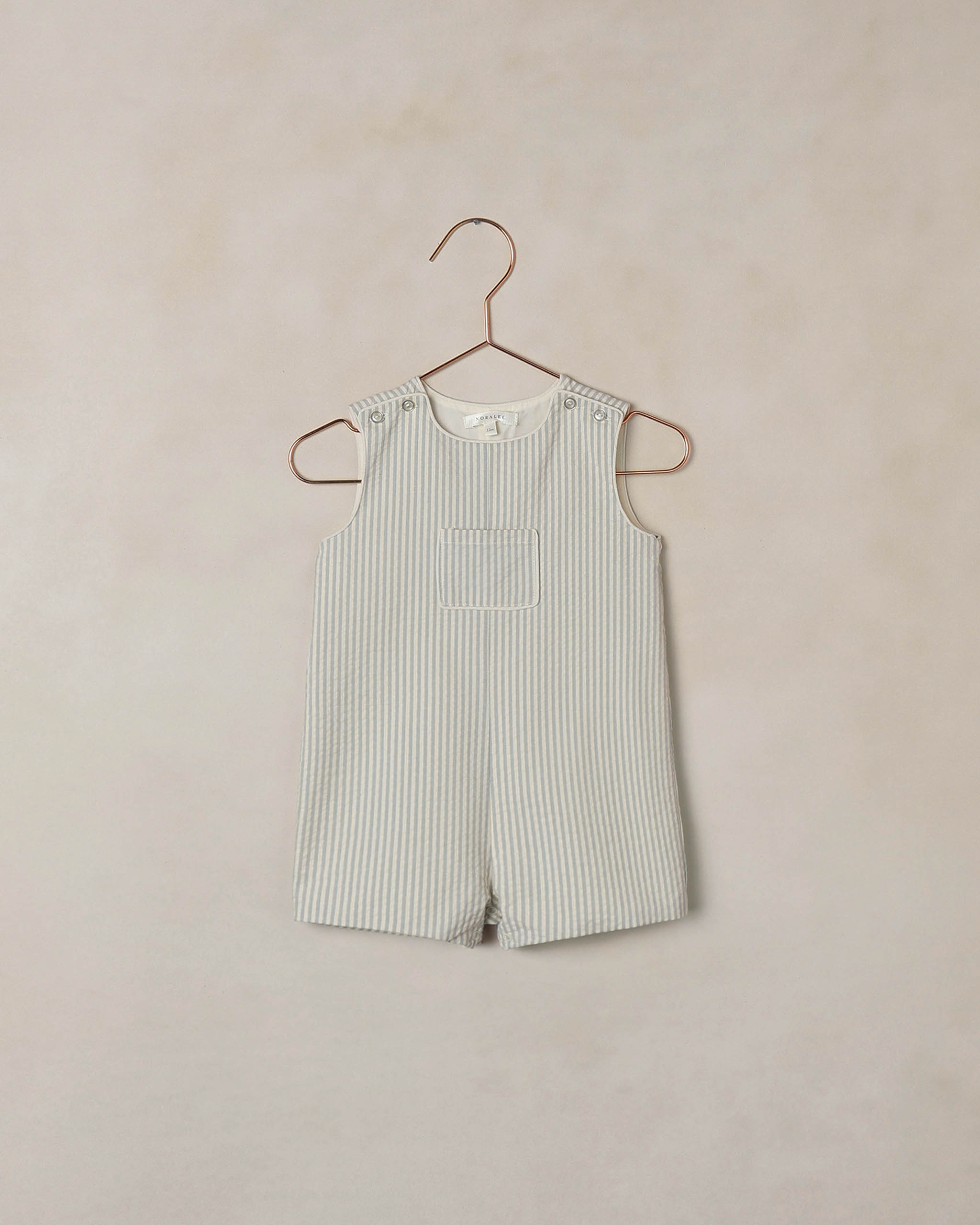 Striped romper on a hanger against a beige background