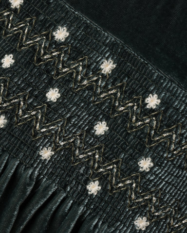 A close up of a green velvet fabric featuring a smocked bodice.